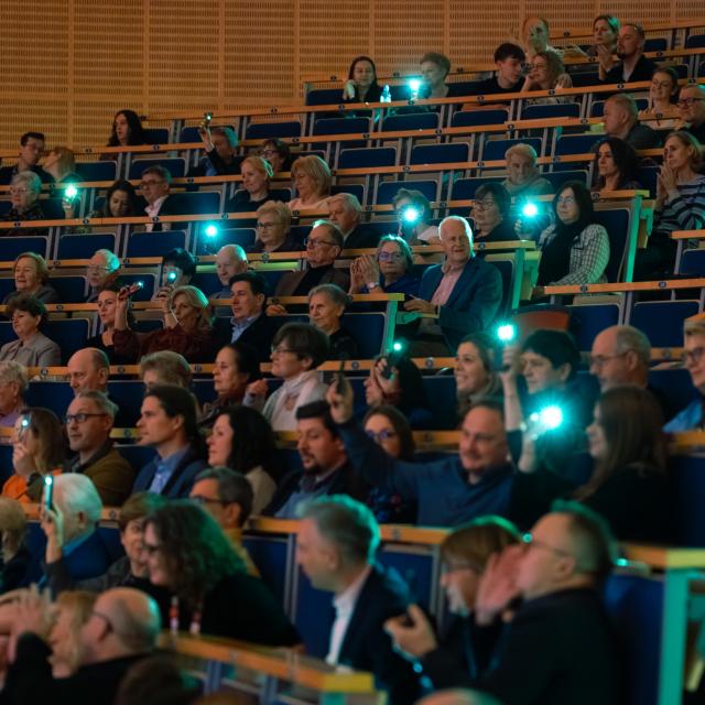 Widownia aktywnie uczestniczy w koncercie, rozświetlając salę latarkami telefonów.